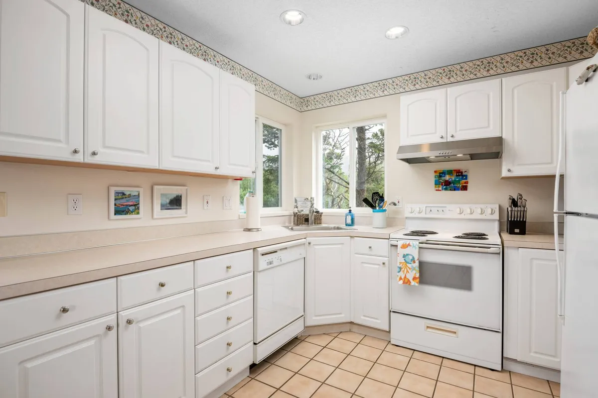 A cozy kitchen featuring white cabinetry, a window with a scenic view, stainless steel appliances, and a decorative backsplash. The space is well-lit and offers an inviting atmosphere for cooking and gathering.