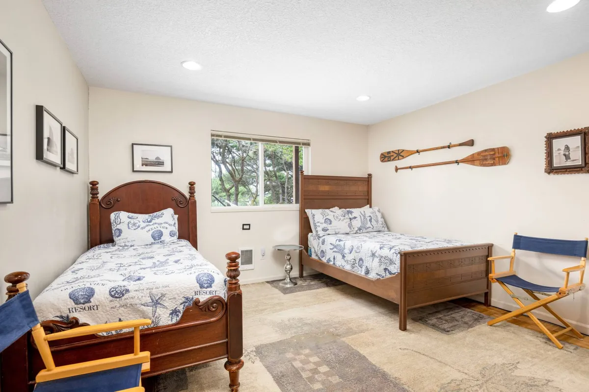 A comfortable bedroom featuring two neatly made beds, a window streaming in natural light, and decorative paddles on the wall. The space feels calm, flexible, and family-friendly, with coastal touches in the decor.