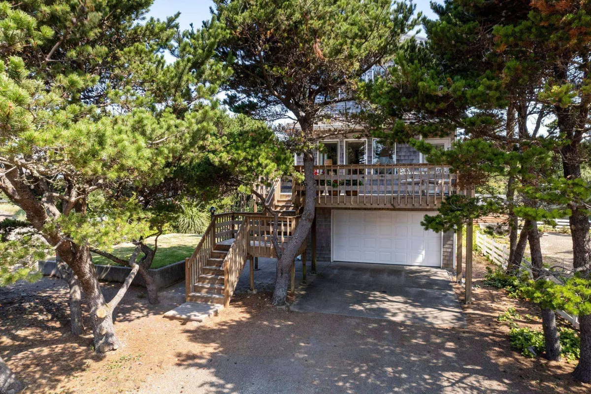 This image features a wooden deck surrounded by lush greenery, attached to the home with a direct view that hints at proximity to the ocean. The scene is evocative of tranquil outdoor moments, with plenty of privacy offered by the foliage. The deck is an inviting space for evening relaxation or enjoying a glass of wine at sunset.
