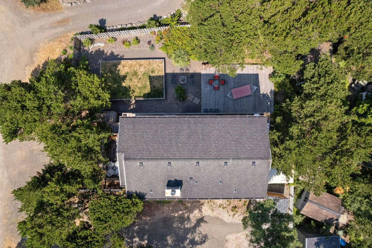 A welcoming exterior view of the house, showcasing a spacious patio area with red chairs, lush greenery, and an open lawn. The setting invites families to relax outdoors, celebrate special occasions, or play games together while soaking in the peaceful seaside environment.