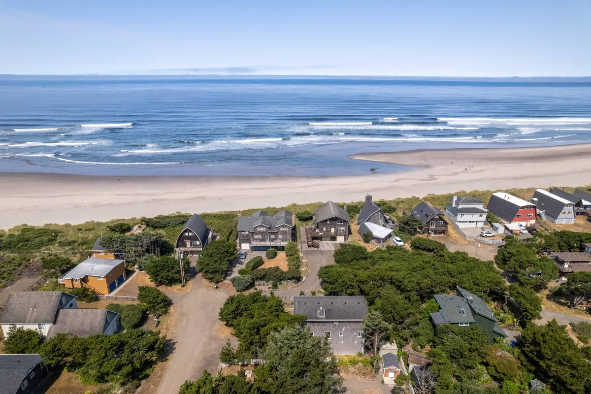 A wide, sandy beach stretches toward the ocean, with charming beach houses lining the edge and a winding pathway leading directly to the shore. The scene is filled with inviting open space, perfect for building sandcastles, flying kites, or venturing out for a seaside adventure with family.