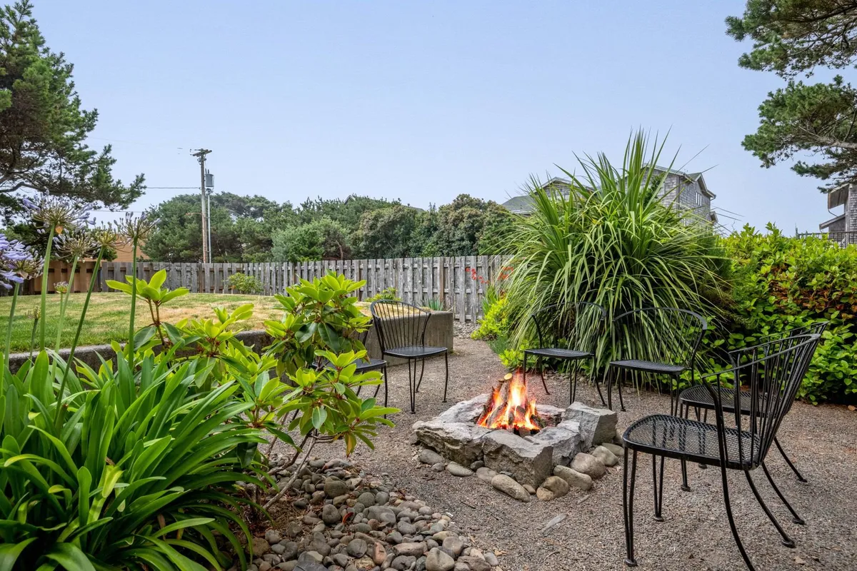 A cozy stone fire pit surrounded by greenery forms the centerpiece of a relaxed outdoor seating area. The setting is perfect for gathering with loved ones to roast s’mores, swap stories, and stargaze under clear coastal skies as evening falls.