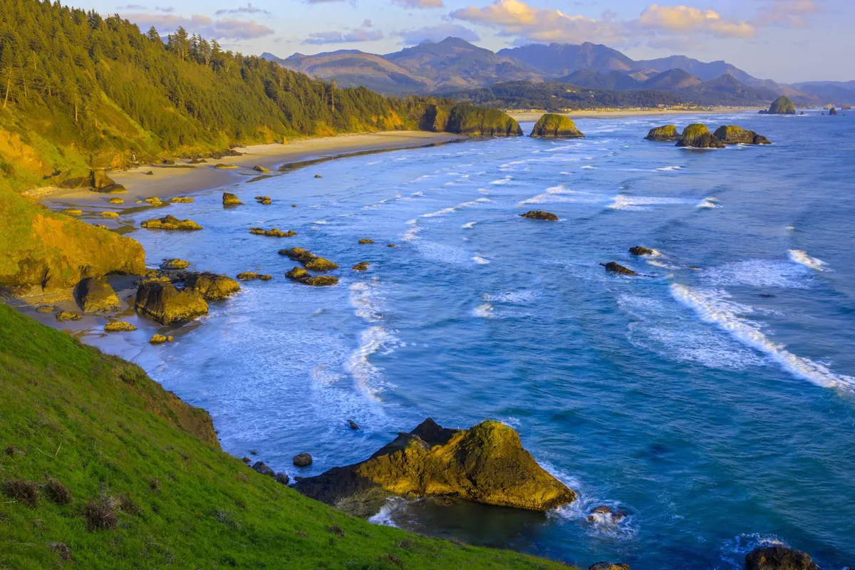 A breathtaking view of the rocky coastline with gentle waves, distant mountains, and green hills. The scene is serene and expansive, capturing the sweeping ocean views and natural beauty that define Tierra del Mar.