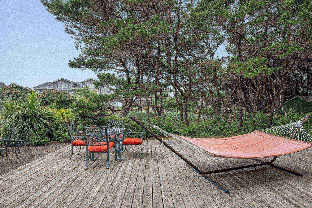 An exterior scene with a hammock gently swaying among greenery, accompanied by an outdoor dining set. The lush surroundings and open sky evoke a sense of peaceful seclusion ideal for summer lounging or al fresco meals.