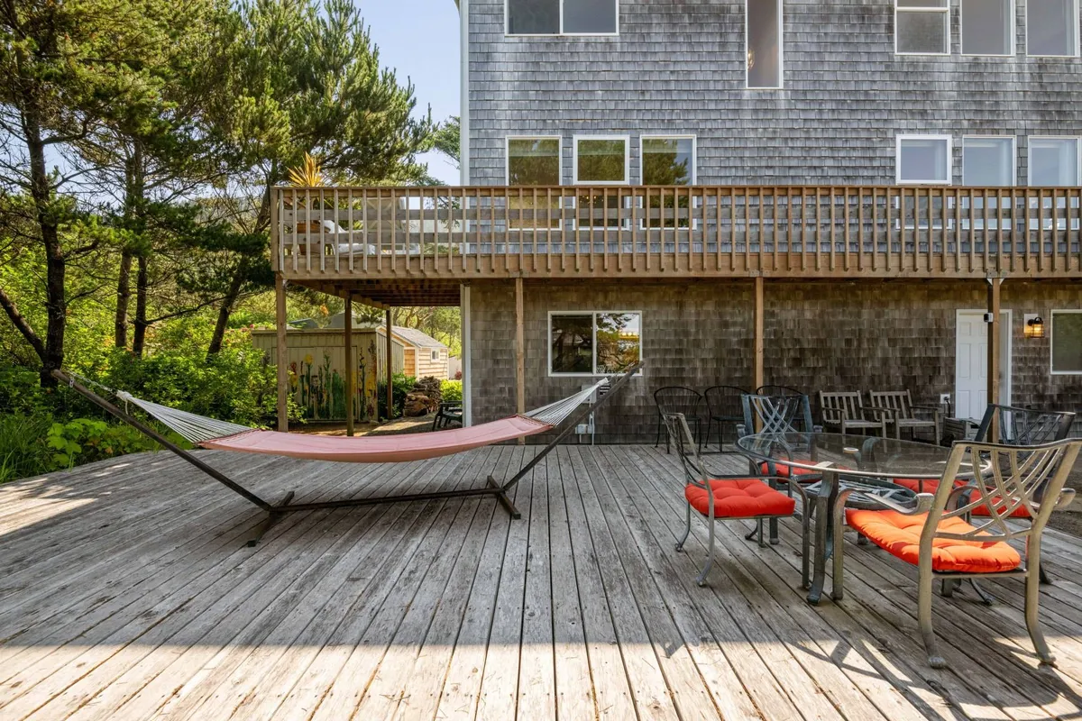 This image showcases a portion of the wraparound deck, featuring a cozy hammock nestled among surrounding trees. The deck also offers seating areas inviting guests to relax, read a book, or enjoy the tranquil natural backdrop. Soft evening lighting suggests the potential for sunset views and starlit conversations.
