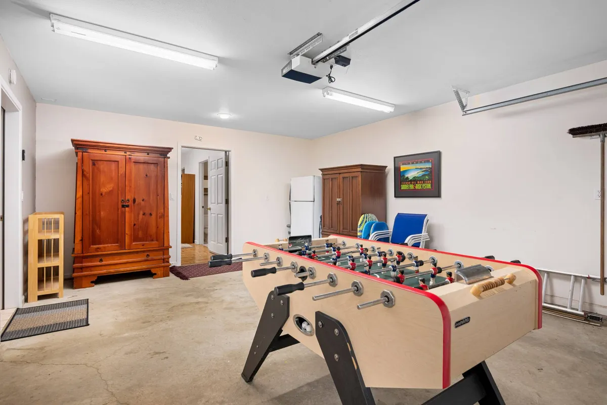 Inside the garage, a foosball table stands ready for friendly competitions. The space is functional yet inviting, with blue chairs for spectators and a wooden armoire providing additional storage. The relaxed, playful vibe invites guests to have fun regardless of the weather.